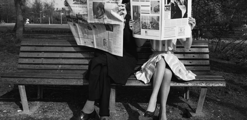 Een tweetal op een bank leest de krant, zwartwitfoto